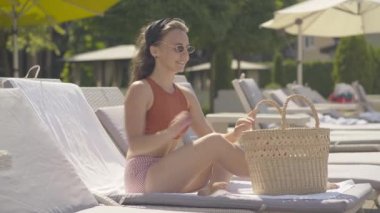Güneş gözlüklü, kendine güvenen genç bir kadının okumak ve dinlenmek için kitap alıp uzanması. Güzel esmer beyaz bir kızın portresi lüks bir tatil köyünde dinleniyor..