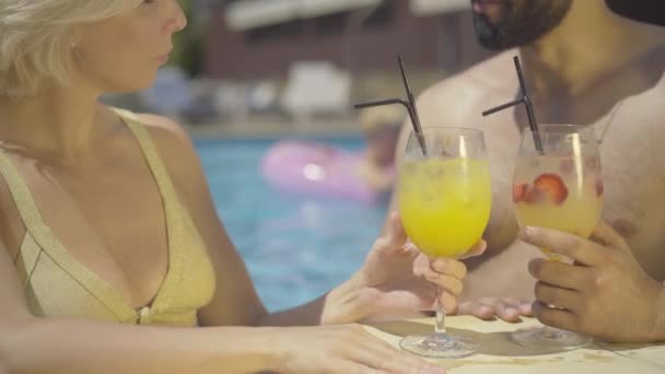 Gros plan de femme blanche blonde cliquetis lunettes avec homme barbu dans la piscine d'eau. Heureux jeune couple multiethnique reposant sur des vacances dans un complexe de luxe. Touristes profitant d'une journée ensoleillée en plein air. — Video