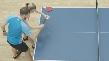 Beyaz erkek ve kadının pinpon oynadığı en iyi manzara. Spor salonunda masa tenisi oynamak için spor eğiten bayan koç. Sağlıklı yaşam tarzı, spor anlayışı.