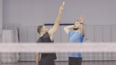 Kişisel antrenörle kavrayış tekniği ve duruş pratiği yapan konsantre sporcu. Beden eğitiminde kendine güvenen beyaz adamların portresi. İçeride badminton oynayan iki adam..