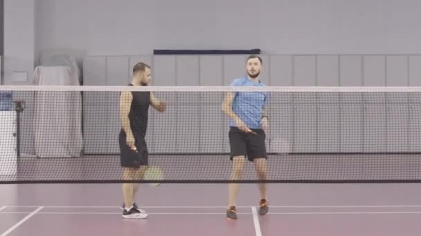 Weitschuss von gut aussehenden athletischen Sportlern, die auf dem Indoor-Court in der Turnhalle trainieren. Positiver junger Mann aus dem Kaukasus trainiert Federball als persönlicher Trainer. — Stockvideo