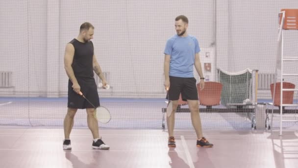 Szerokie ujęcie sportowców trenujących ruch dłoni badmintona w pomieszczeniach. Portret pozytywnych mężczyzn rasy kaukaskiej trenujących grę sportową w siłowni. Przystojni dorośli faceci w sportowej odzieży ćwiczą. — Wideo stockowe