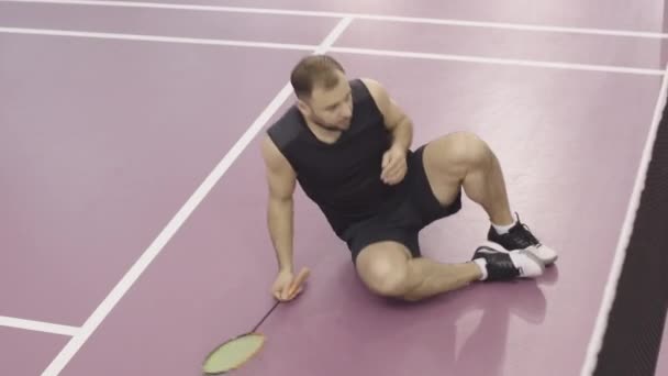 Angle vue du dessus du sportif caucasien épuisé couché sur le sol de la salle de gym et se reposant après un match de compétition. Portrait large de jeune homme fatigué formation jeu de badminton à l'intérieur. — Video