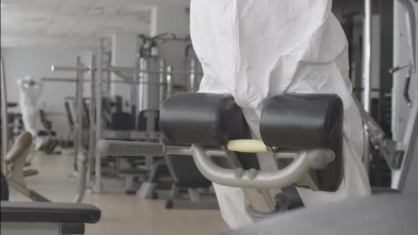 身穿防护服和呼吸器的女运动员在健身房的器械上训练背部肌肉。白人妇女在科维德-19隔离室内锻炼的肖像。Coronavirus流行病概念. — 图库视频影像