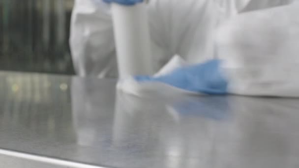 Mujer irreconocible con guantes protectores azules rociando desinfectante y frotando equipos deportivos en el gimnasio. Empleada en traje antiviral blanco desinfectando club deportivo en pandemia de coronavirus . — Vídeo de stock