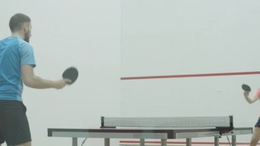 Beyaz bir adam ve kadın içeride masa tenisi oynuyorlar. Spor salonundaki kendine güvenen sporcu ve sporcu kadın eğitiminin portresi. Spor kulübünde atletik insanlar pinpon oynuyor..