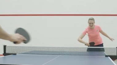 Tanınmayan bir sporcuyla pinpon oynayan pozitif kadın portresi. Neşeli, genç, beyaz bir kadın raketle topa vurup konuşuyor. Spor salonunda masa tenisi antrenmanı yapan neşeli sarışın kız..