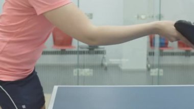 İçeride pinpon oynayan tanınmayan sporcu kadının yan görüntüsü. Beyaz bir kadın raketle pinpon topuna vuruyor. Beden eğitiminde masa tenisi sporu eğitimi.