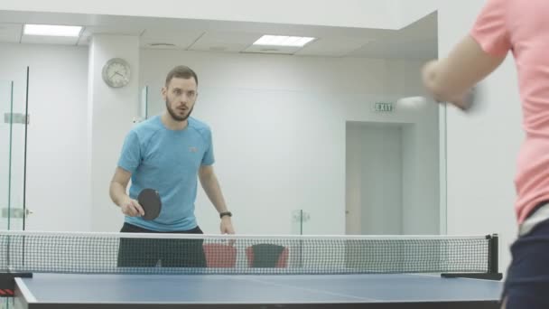 Självsäker koncentrerad idrottsman spelar pingis med oigenkännliga idrottskvinna i gymmet. Porträtt av en vit man spelar bordtennis med kvinnan inomhus. Workout koncept. — Stockvideo