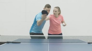 Sarışın kadın Kafkas koç yakışıklı sakallı sporcuya masa tenisi dersi veriyor. Spor salonunda esmer adamı eğiten genç bir kadının portresi. Masa tenisi oyunu.