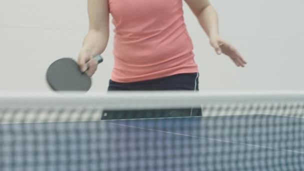 难以辨认的女人在乒乓球网上用球拍击球.年轻的白人女运动员在体育馆里训练乒乓球。女孩在室内运动的前景. — 图库视频影像
