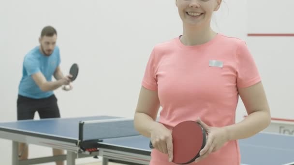 Femme souriante méconnaissable montrant le geste OK comme un homme caucasien flou s'entraînant au tennis de table en arrière-plan. Portrait d'une jeune sportive se faisant passer pour une sportive pratiquant le ping-pong. — Video
