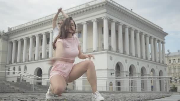 Чувственный современный танец красивой брюнетки белой девушки с танцовщицей, исполняющей танец робота на заднем плане. Две молодые кавказские женщины танцуют на городской площади. Уличный образ жизни. — стоковое видео