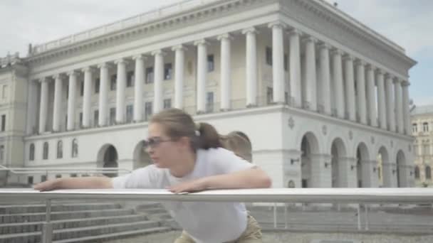 Portrét mladé radostné bělošky v slunečních brýlích tančící robot tanec na náměstí. Bruneta hezká mladá žena provádějící moderní tanec na pozadí starověké evropské budovy. — Stock video