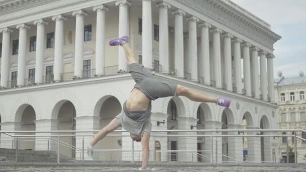 Fiducioso ballerino allegro pausa in piedi su una mano con le gambe alzate. Ampia ripresa di forte uomo caucasico che esegue movimento di danza atletica sulla piazza della città il giorno d'estate. Stile di vita urbano. — Video Stock