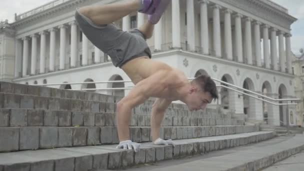 Kamera zbliża się do pewnego siebie wesołego człowieka stojącego na rękach na miejskich schodach i poruszającej się głowie. Portret sportowca kaukaski break tancerz szkolenia na świeżym powietrzu w letni poranek. — Wideo stockowe