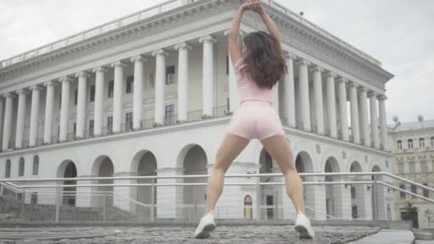 Vue d'ensemble de la belle danseuse twerk se produisant à l'extérieur sur la place de la ville. Portrait de femme blanche brune joyeuse dansant danse moderne à l'arrière-plan de l'ancien bâtiment européen. — Video