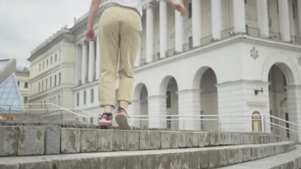 Молодая веселая девушка в наушниках поднимается по городской лестнице и танцует робот-танцор. Портрет радостной кавказской молодой женщины, выступающей на городской площади под открытым небом. Арт-перформанс. — стоковое видео