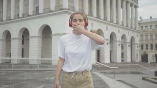 Kulaklık takmış, ağzı kapalı robot dansı yapan çekici bir kız resmi. Şehir merkezinde sahne alan neşeli beyaz bir genç kadının portresi. Modern sanatlar, yaşam tarzı. — Stok video