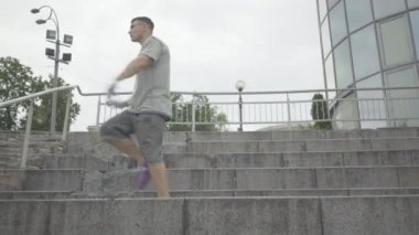 Kentin merdivenlerinde kendinden emin beyaz bir gencin ters takla atması. Yakışıklı esmer dansçının geniş açılı portresi yaz günü şehir caddesinde sergilenecek..