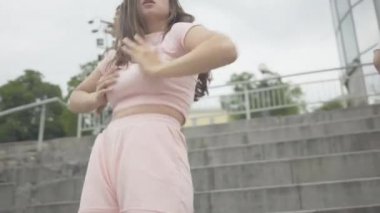 Güneş gözlüklü, robot dansı yapan neşeli kıza dans eden ve fotoğraf makinesi veren şehvetli beyaz kadın. Bir grup neşeli erkek ve kadın dansçı şehir meydanında eğleniyor..