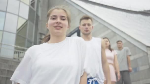 Portret czterech radosnych białych młodych tancerzy stojących w rzędzie na miejskich schodach i poruszających się dłoniach. Wesoły młody mężczyzna i kobieta tańczący taniec nowoczesny na świeżym powietrzu. — Wideo stockowe