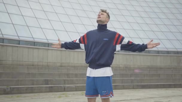 Självsäker break dansare utför modern dans i centrum på molnig dag. Porträtt av stilig ung vit man njuter av frihet utomhus. Sorglös livsstil, lycka. — Stockvideo