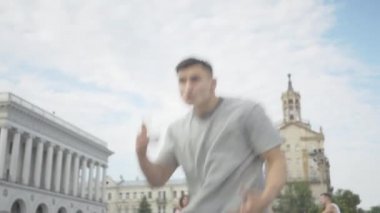 Güneşli şehir meydanında kendine güvenen genç esmer adamın enerjik dansı. Arka planda dans eden arkadaşlarıyla birlikte dans eden ciddi bir beyaz erkek dansçının portresi.