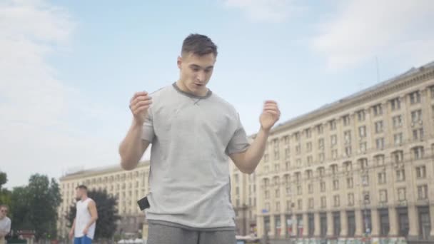 Plano medio de morena hombre confiado bailando danza robot en la plaza de la ciudad con amigos. Retrato del guapo joven bailarín caucásico disfrutando de la actuación callejera en el día de verano al aire libre . — Vídeos de Stock