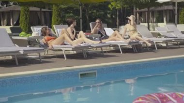 Pozitif genç bir bayanın güneş altında arkadaşlarıyla konuştuğu geniş bir açı. Lüks tatil beldelerinde dedikodu yapan mutlu beyaz kadın portresi. Dişi turistler dışarıda dinleniyor..