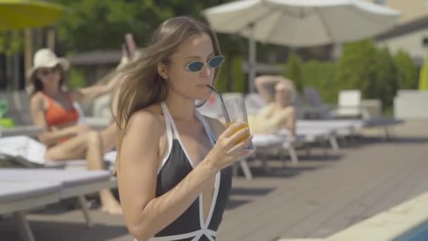 Glada brunett kvinna med cocktail kysser enhörning simning ring på solig dag. Sidovy porträtt av glada kaukasiska turist vilar på sommaren resort. Turismbegreppet. — Stockvideo