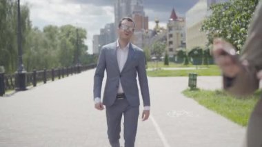 Kendine güvenen zarif iş adamının resmi takım elbiseli ve güneş gözlüklü portresi. Şehir caddesinde arkadaşlarıyla buluşup onlarla birlikte gidiyor. Genç, pozitif, beyaz bir adam. Dışarıda erkek ve kadınları selamlıyor..