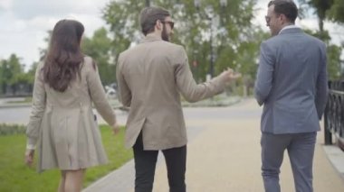 Kamera, şehir caddesi boyunca scooterlara doğru yürüyen zarif beyaz erkek ve kadınları takip ediyor. Kendinden emin genç erkek ve kadın motosikletçilerin gezinip konuşmalarının arka görüntüsü..