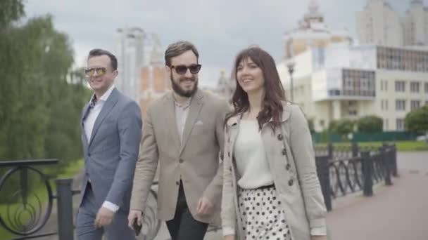 Средний снимок счастливой улыбающейся группы людей, идущих по городской улице и разговаривающих. Позитивные кавказские мужчины и женщины прогуливаются на свежем воздухе в летний день и болтают. — стоковое видео