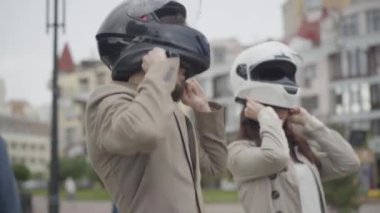 Şehrin caddesinde kask takan kendine güvenen beyaz motorcular. Bulutlu bir yaz gününde yarışa hazırlanan genç erkek ve kadın portresi. Etkin yaşam tarzı kavramı.