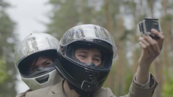 Souriant heureux motards dans les casques de tir selfie vidéo tout en roulant sur la moto. Portrait d'homme et de femme caucasiens conduisant scooter par temps nuageux à l'extérieur. Caméra zoom arrière. — Video