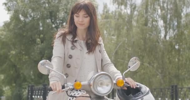 Retrato de mujer morena positiva disfrutando del día de verano al aire libre sentada en bicicleta. Encantadora hermosa dama caucásica en scooter mirando hacia otro lado y sonriendo. En cámara lenta. Sede del cine 4k ProRes. — Vídeo de stock