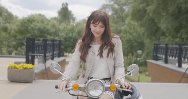 Encantadora morena caucásica sentada en moto y sonriendo. Retrato de hermosa hermosa dama disfrutando del día de verano al aire libre. En cámara lenta. Sede del cine 4k ProRes. — Vídeo de stock