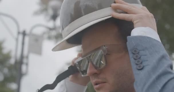 Boční pohled zblízka sebevědomý pozitivní muž, který si nasazuje helmu na kole ve zpomaleném filmu a usmívá se. Portrét pohledného bělocha, který si užívá deštivého letního dne venku. Cinema 4k ProRes HQ.