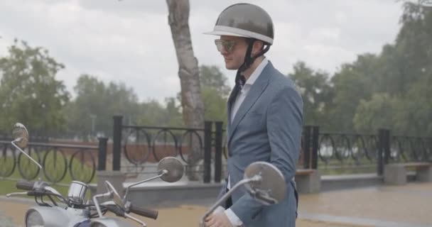 Lento de hombres y mujeres seguros sentados en scooters al aire libre bajo la lluvia. Retrato de ciclistas caucásicos en ropa formal, casco y gafas de sol posando en motocicletas. Sede del cine 4k ProRes. — Vídeos de Stock