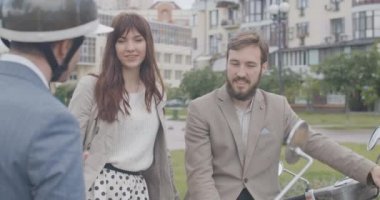 Bisiklet kasklı, tanınmayan bir adamla konuşan beyaz bir çiftin portresi. Mutlu esmer kadın ve sakallı adam arkadaşlarıyla motosiklette oturuyormuş gibi sohbet ediyorlar. Yavaş ol. Sinema 4k ProRes Merkezi.