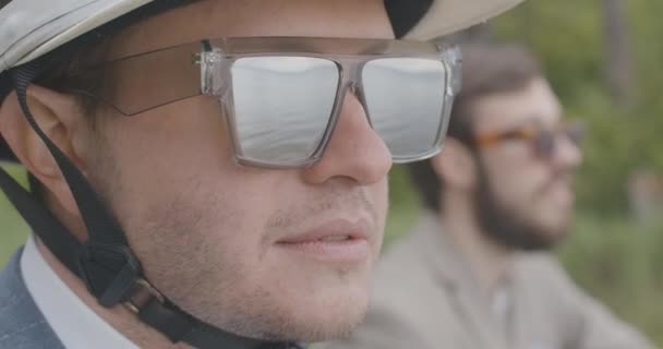 Κοντινό πλάνο πρόσωπο του νεαρού με αυτοπεποίθηση με γυαλιά ηλίου και κράνος χαμογελώντας σε αργή κίνηση. Πορτρέτο του χαρούμενου αρσενικού ποδηλάτη με θαλασσινό ποτάμι ή λίμνη αντανακλώντας σε γυαλιά. Αργοπορημένη. Κινηματογράφος 4k ProRes HQ. — Αρχείο Βίντεο