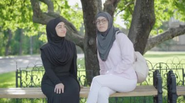 Açık havada bankta oturan ve konuşan iki Müslüman kadının portresi. Parkta ya da üniversite bahçesinde güneşli bir yaz gününün tadını çıkaran pozitif genç kız öğrenciler. Yaşam tarzı kavramı.