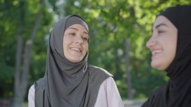 Neşeli genç Müslüman kadın ela gözlü arkadaşlarıyla konuşuyor ve gülüyor. Açık havada güneşli bir günde tesettürlü kızla eğlenen tesettürlü güzel bir kadının portresi. Neşe kavramı.