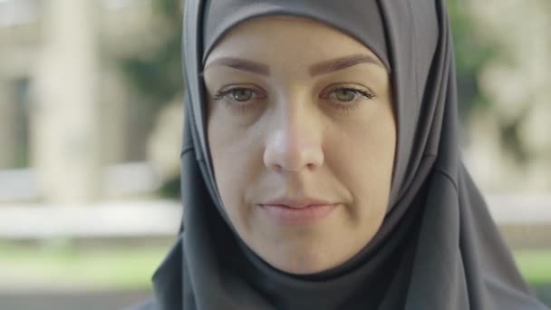 Cara de cerca de la mujer musulmana atractiva y confiada en el hijab mirando la cámara al aire libre. Retrato de un estudiante inmigrante serio posando en un día soleado en el patio de la universidad. Educación internacional. — Vídeo de stock