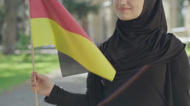 Onherkenbare gelukkige moslimimmigrant poseert met Duitse vlag op zonnige dag buiten. Lachende jonge vrouw in traditionele hijab studeert in Europa. Begrip internationaal onderwijs, uitwisseling van studenten. — Stockvideo
