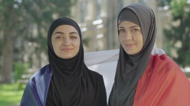 Avrupa 'da üniversite bahçesinde poz veren iki mutlu Müslüman göçmene yakın çekim. Geleneksel tesettürlü gülümseyen kadın portresi yurtdışında eğitim görüyor. Öğrenci değişim konsepti.
