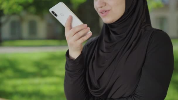 Mujer musulmana irreconocible usando smartphone para la grabación de mensajes de audio. Sonriente joven dama confiada que se comunica en línea. Centrado en la mano femenina sosteniendo el teléfono. Concepto de tecnologías modernas. — Vídeo de stock