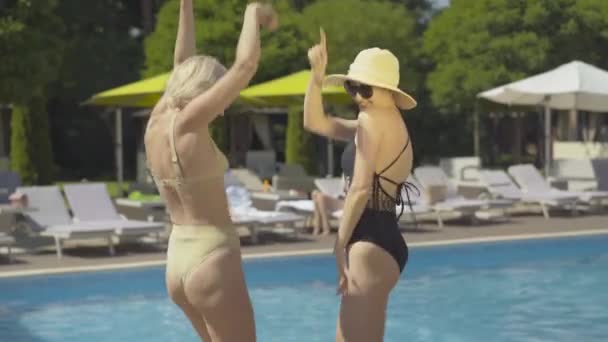 Foto media de mujeres adultas caucásicas alegres bailando en la piscina en un día soleado. Retrato de felices turistas adineradas disfrutando de vacaciones en un lujoso resort. — Vídeos de Stock