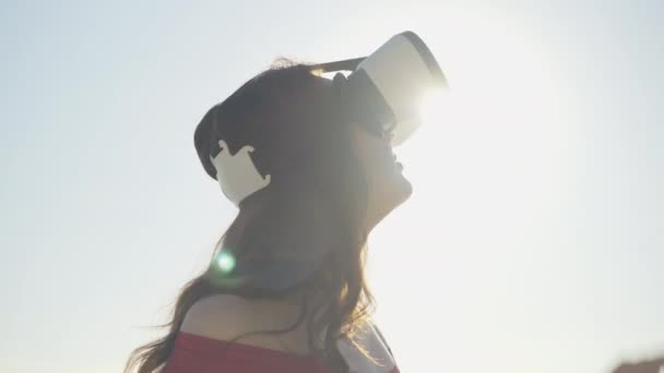 Närbild av glad ung brunett kvinna i VR-glasögon stående i solstrålar utomhus. Porträtt av leende positiv vit dam med hjälp av VR-googlar på solig sommardag. Fritid och livsstil. — Stockvideo